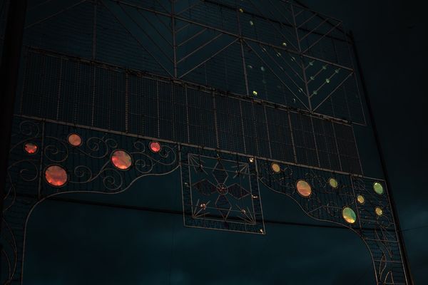 Un arco de luces de fiesta todavía apagado, con sus bombillas de colores contra el cielo azul oscuro.