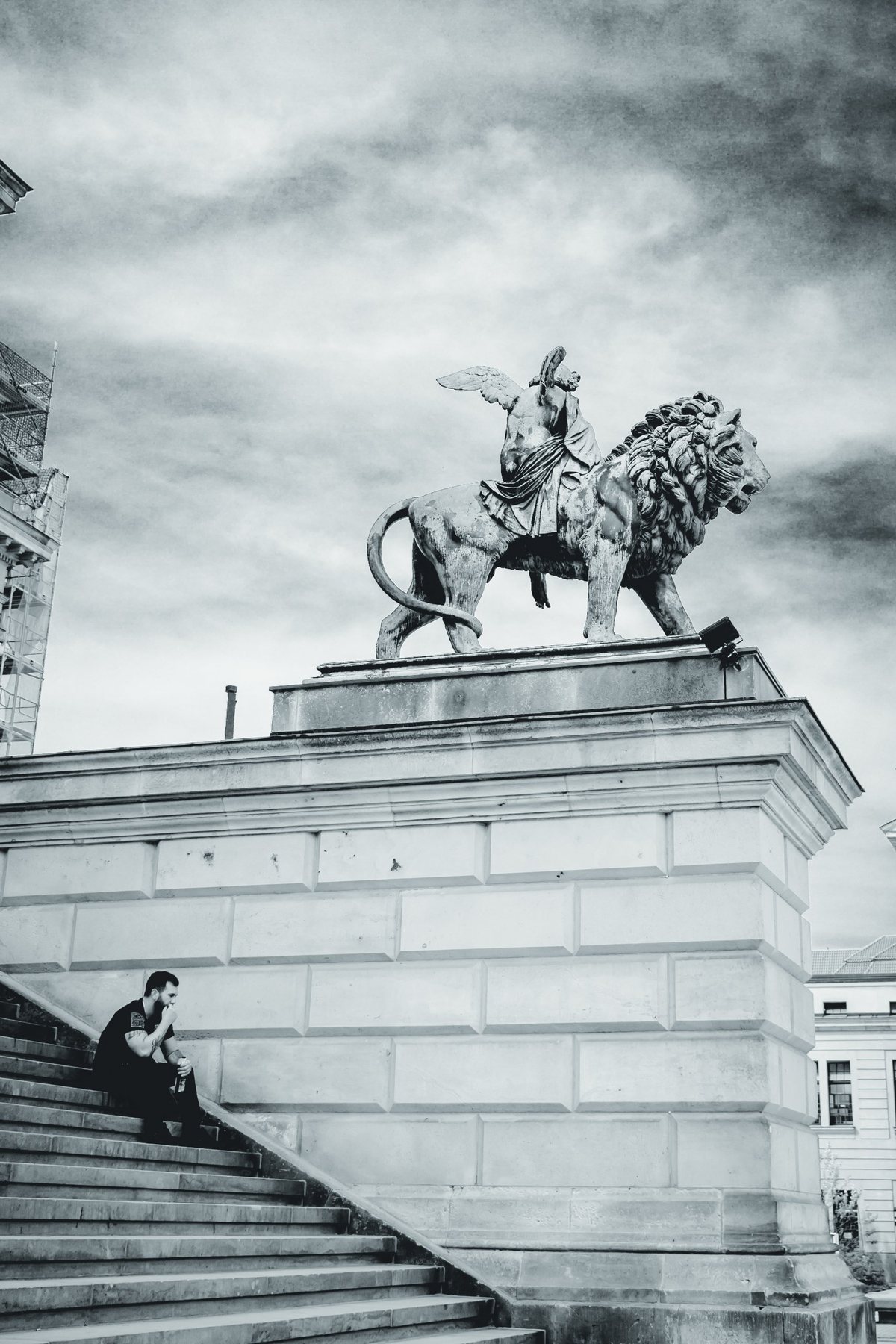 Un hombre descansa en la escalinata de la Konzerthaus mientras la figura alada y su león vigilan desde arriba.