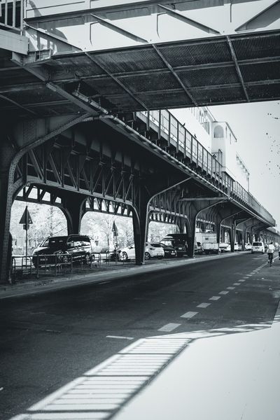 Las arcadas de hierro remachado del metro elevado, con la sombra de la barandilla dibujada en la acera.