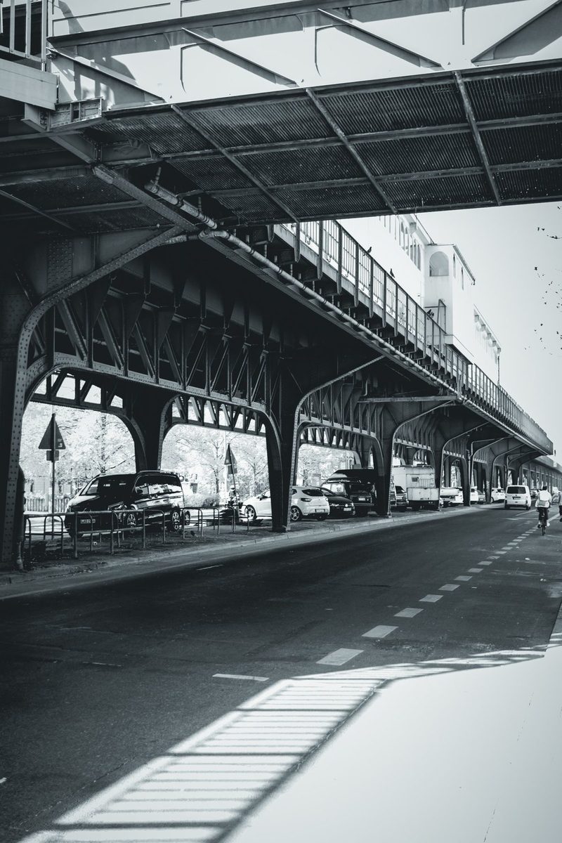 The riveted iron arches of the elevated railway, with the shadow of the railing drawn on the pavement.