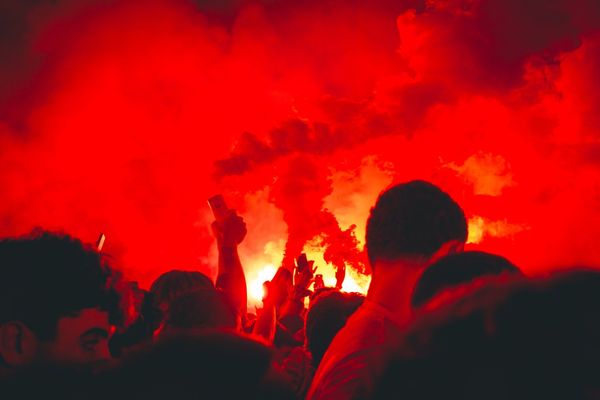 Brazos y móviles alzados frente a las bengalas, con todo el cielo convertido en humo rojo.