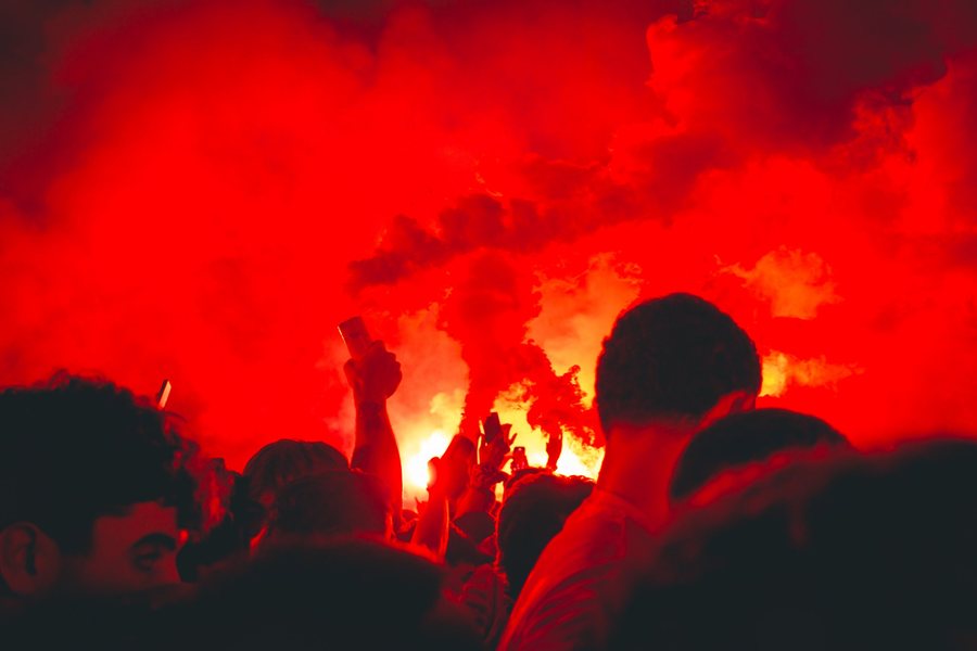 Brazos y móviles alzados frente a las bengalas, con todo el cielo convertido en humo rojo.