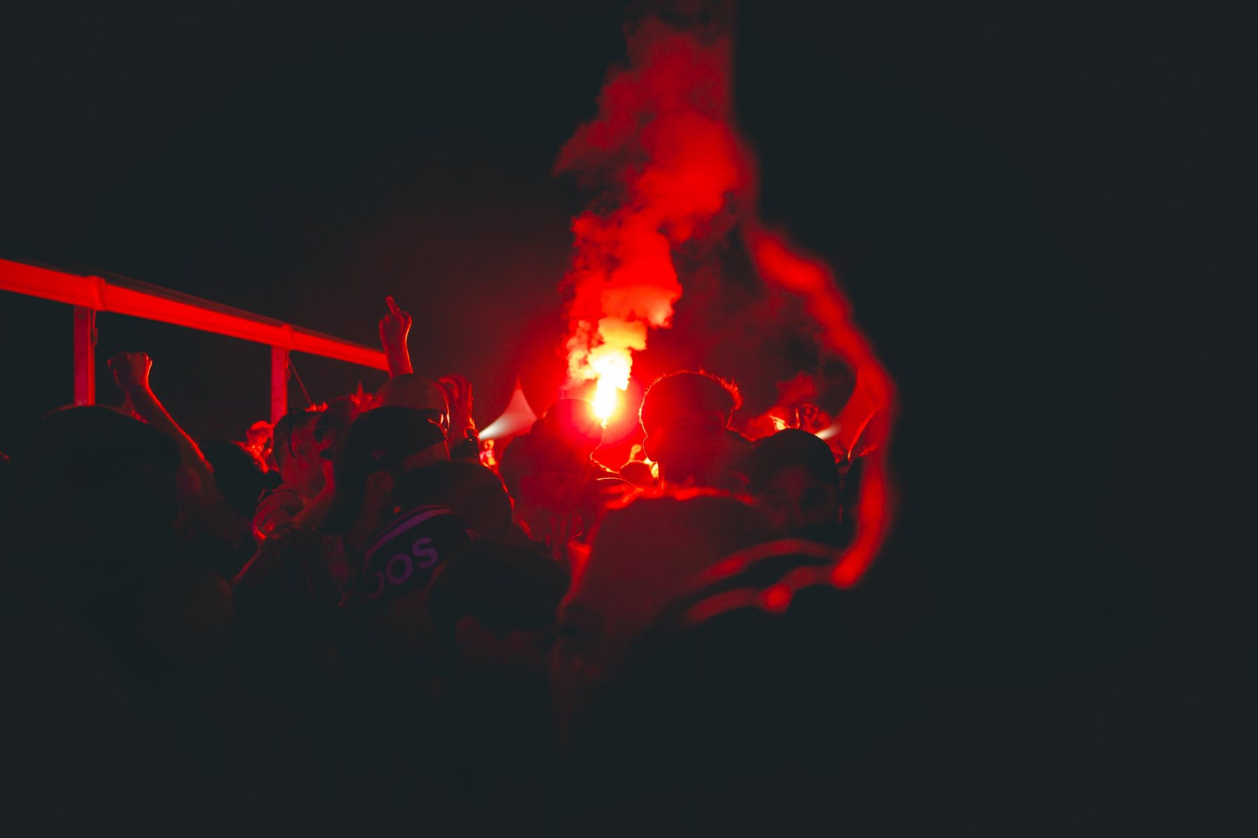 Una bengala ilumina las siluetas de la afición en mitad de la noche.