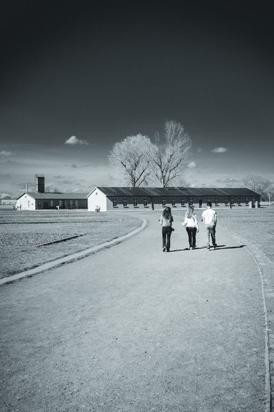 Three visitors walk towards the barracks across the former camp grounds.