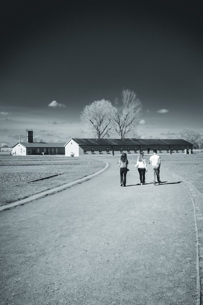 Three visitors walk towards the barracks across the former camp grounds.