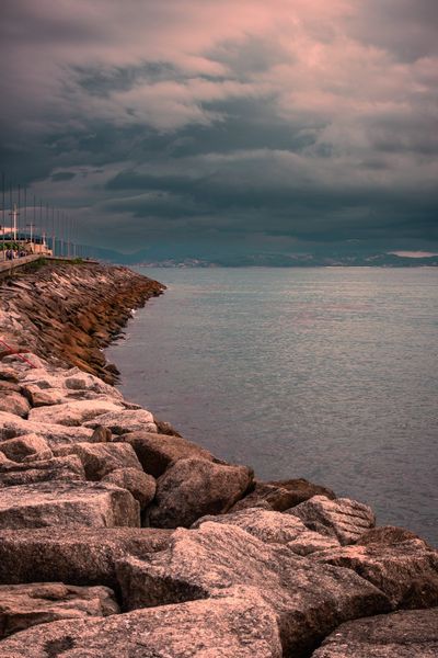 Las rocas del espigón se adentran en el mar gris bajo un cielo cubierto de nubes rosadas.
