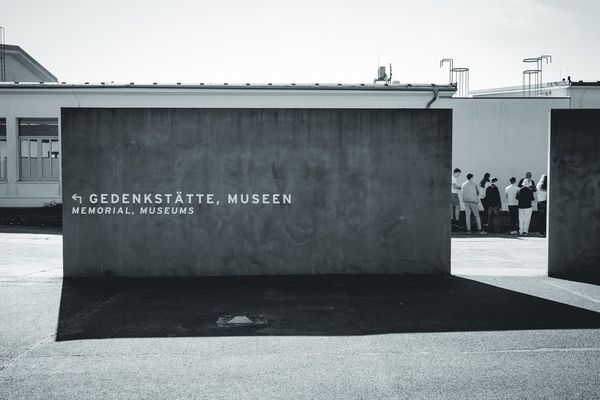 The concrete block pointing the way to the memorial and museums, with a group of visitors in the distance.
