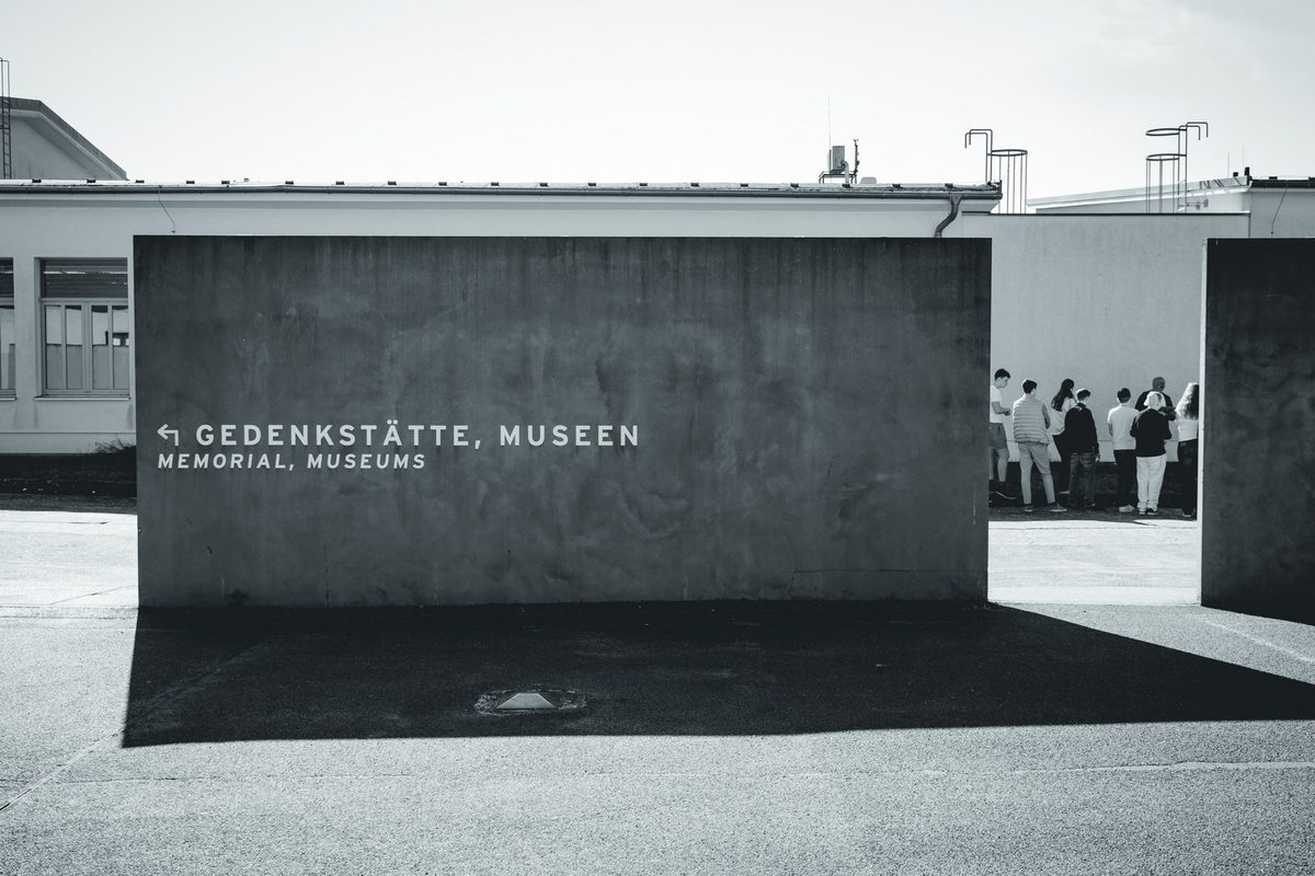 The concrete block pointing the way to the memorial and museums, with a group of visitors in the distance.