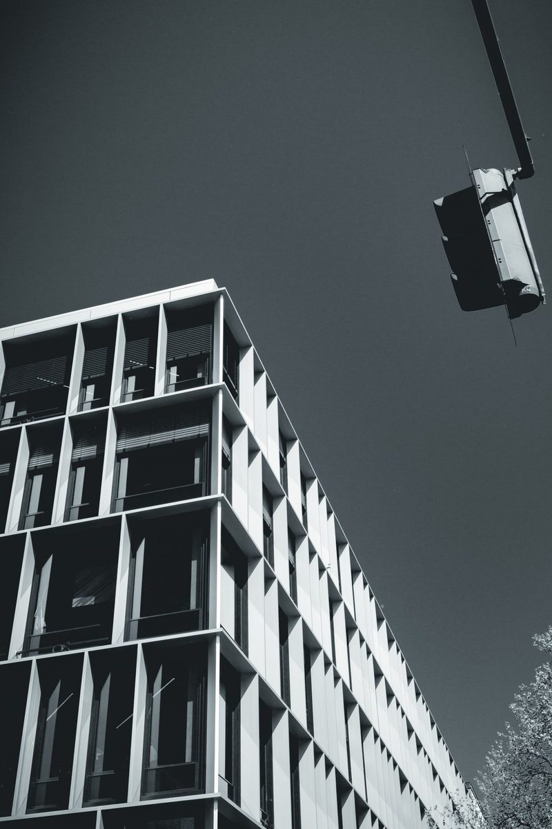 The grid of a modern façade against an almost black sky, and a traffic light hanging on the corner.