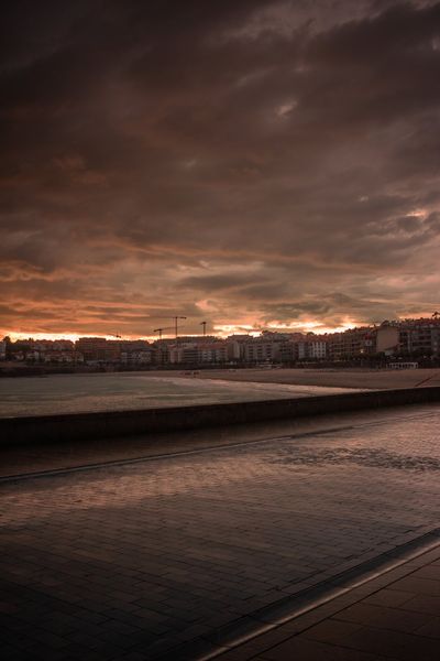 El paseo de Silgar mojado por la lluvia, con los edificios y las grúas recortados contra el ocaso.