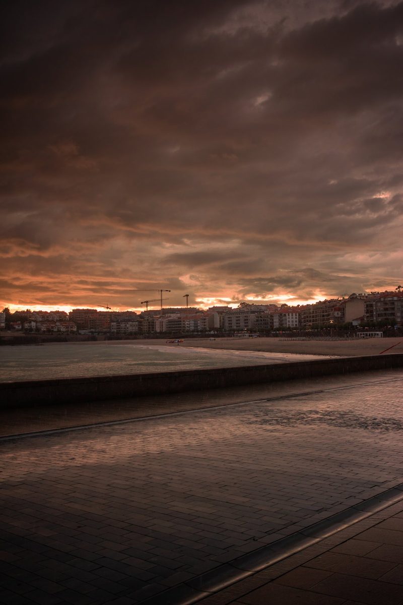 El paseo de Silgar mojado por la lluvia, con los edificios y las grúas recortados contra el ocaso.