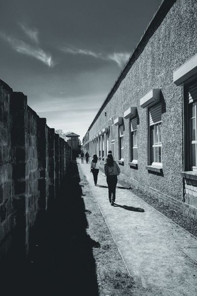 The narrow passage between the camp wall and one of the buildings, with a tower at the end.