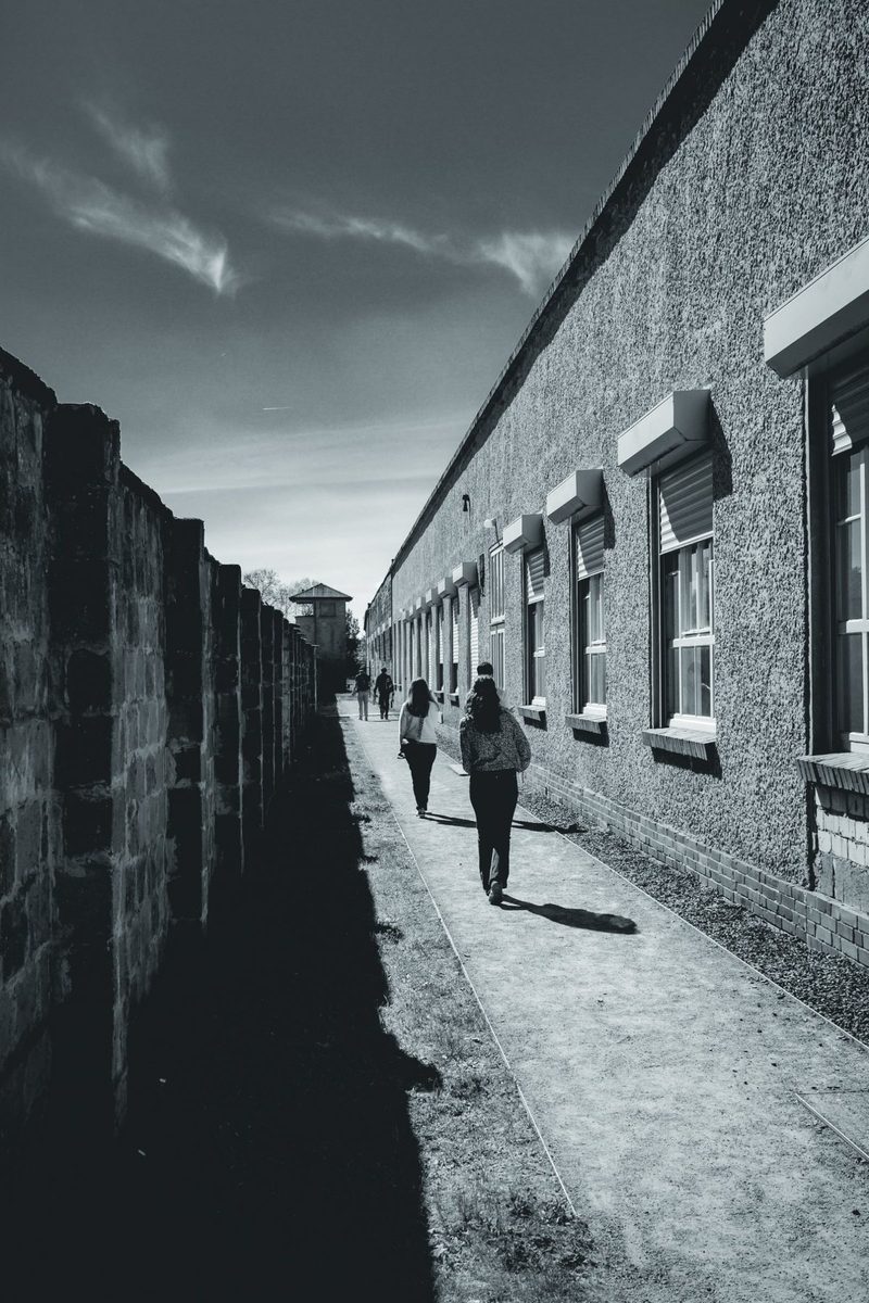 The narrow passage between the camp wall and one of the buildings, with a tower at the end.