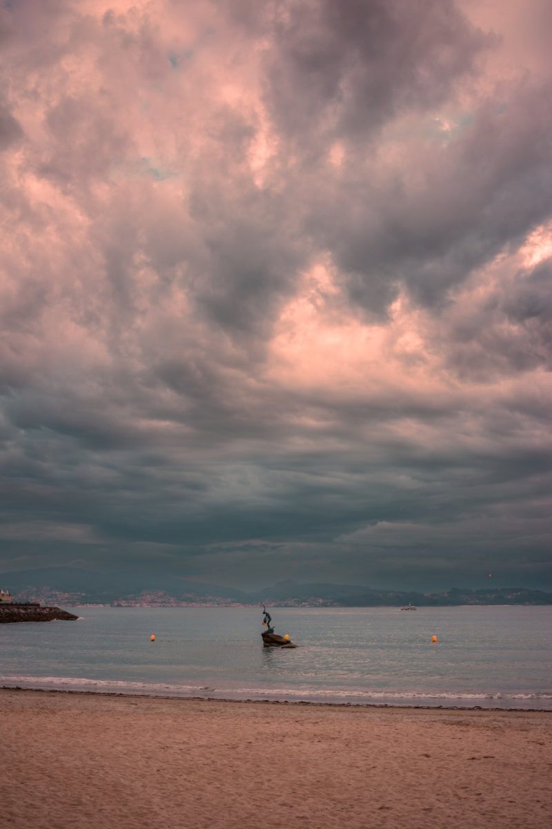 La pequeña estatua de la Madama de Silgar sobre su roca, bajo un cielo de tormenta teñido de rosa.