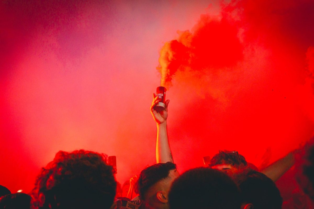 A hand holds up a smoke canister above the crowd while red fills everything.