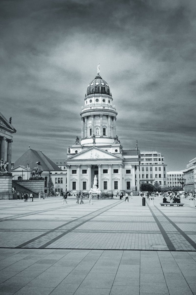 The cobblestones of Gendarmenmarkt lead the eye to the dome, with tiny figures beneath a heavy sky.