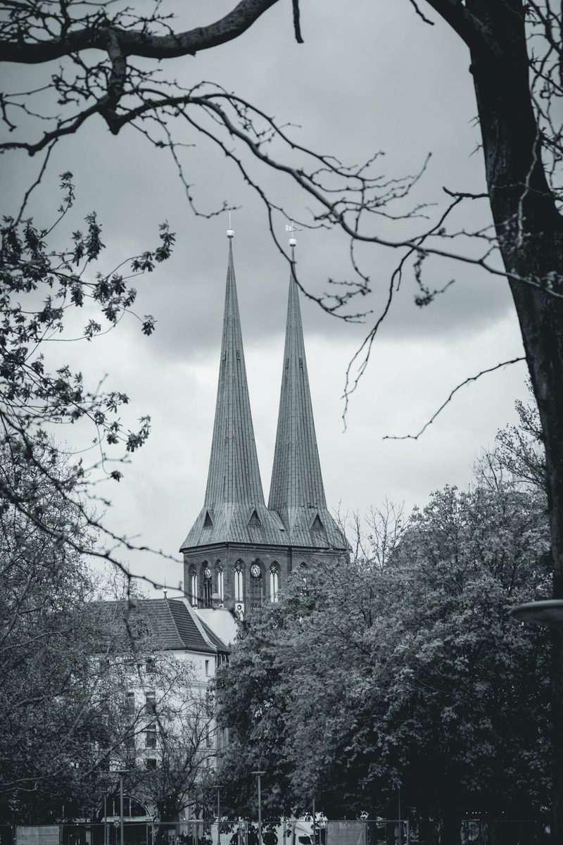 The two spires of the Nikolaikirche rise between spring branches and treetops.