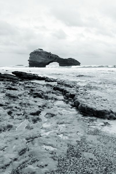 Las rocas de la marea baja conducen la mirada hasta el arco, bajo un cielo cerrado.