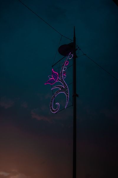 Una mariposa de luces violetas colgada de una farola, contra el cielo azul del anochecer.