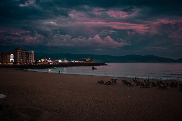 La playa de Silgar al anochecer, con las luces de la fiesta en el paseo y nubes rosas sobre la ría.