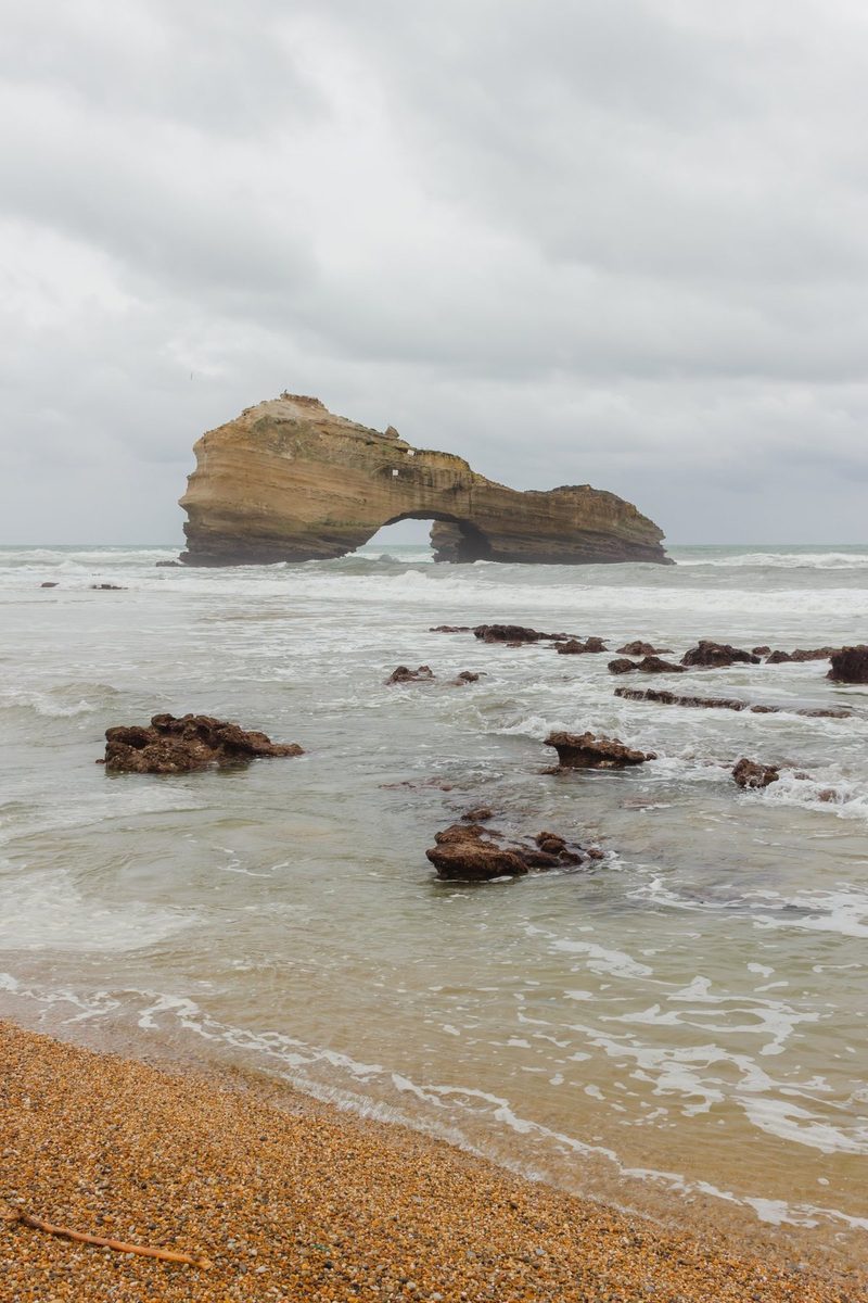 The same shore in colour: golden shingle, greenish water and the arch in the distance.