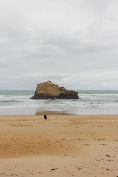 A tiny figure crosses the wet sand towards the rock, under a huge sky.