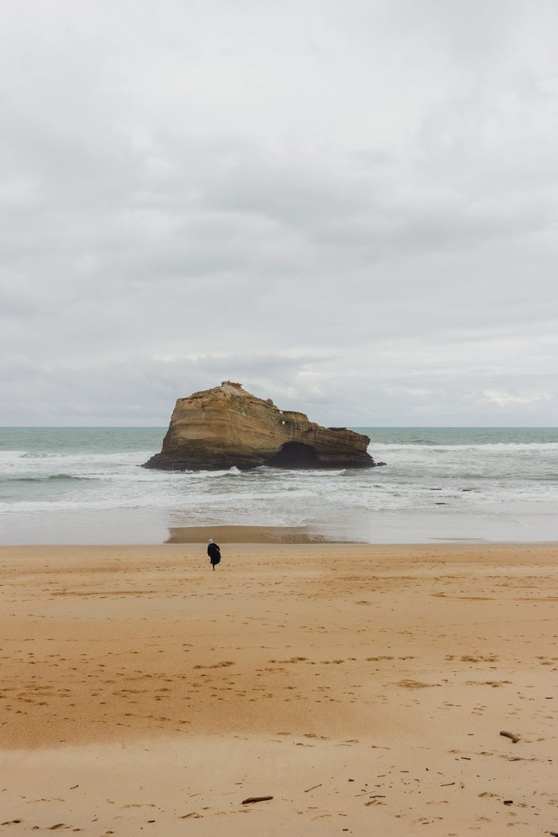 A tiny figure crosses the wet sand towards the rock, under a huge sky.