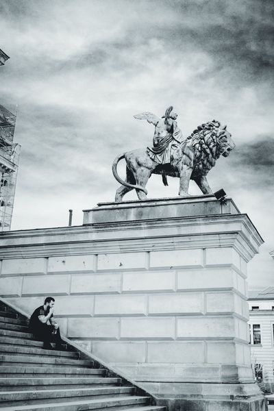 Un hombre descansa en la escalinata de la Konzerthaus mientras la figura alada y su león vigilan desde arriba.