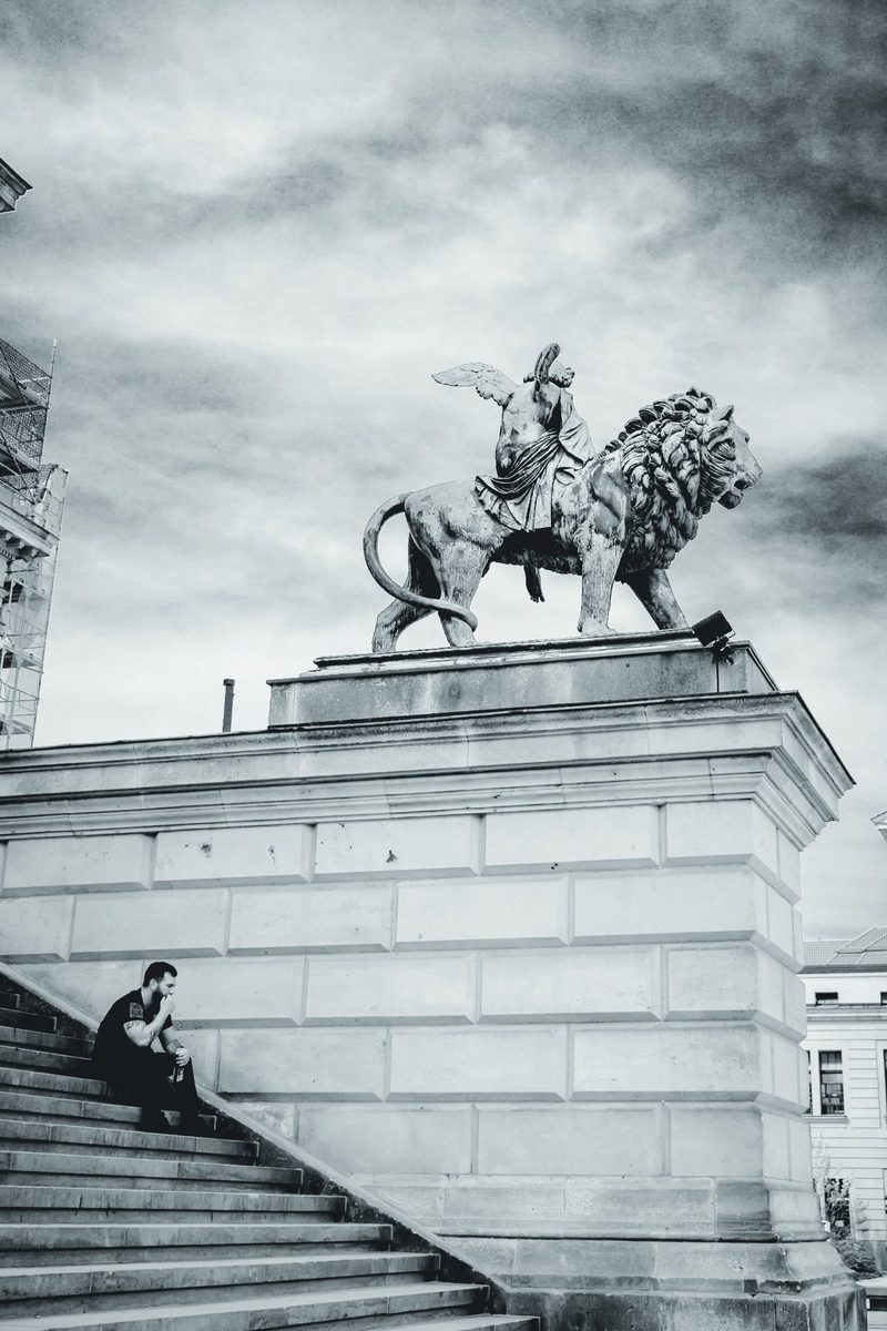 A man rests on the steps of the Konzerthaus while the winged figure and her lion keep watch from above.