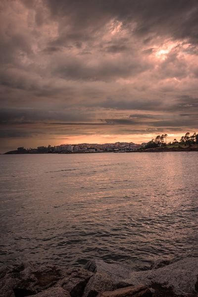 El mar se abre hacia Portonovo bajo un cielo de nubes rosas y una franja de luz en el horizonte.