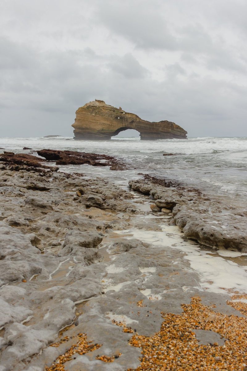 The grey slabs of the beach and the Roche Percée in the distance, among the foam.
