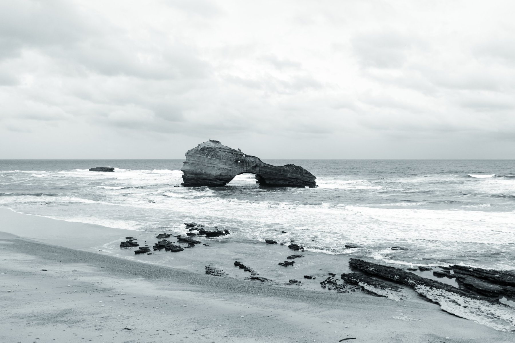 La Roche Percée en el centro del mar revuelto, con la playa y las rocas en primer plano.