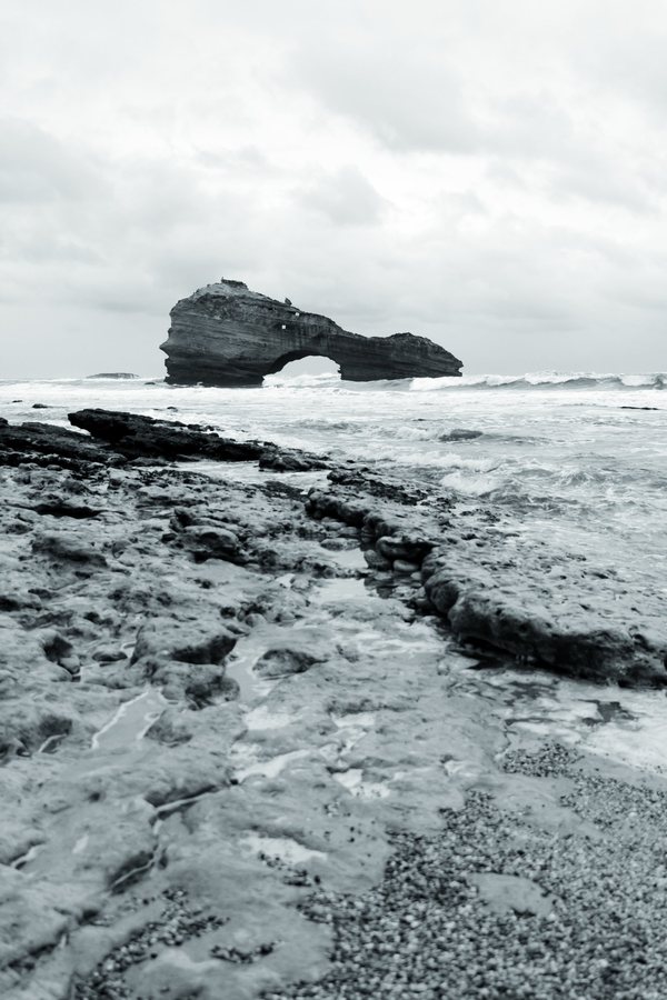 Las rocas de la marea baja conducen la mirada hasta el arco, bajo un cielo cerrado.