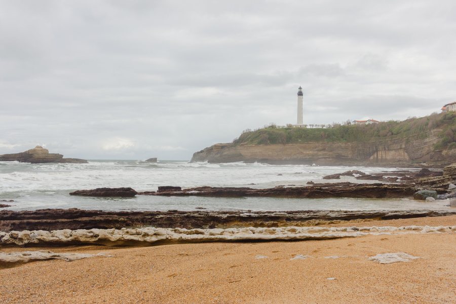 El faro blanco sobre el acantilado, visto desde la playa de arena dorada.