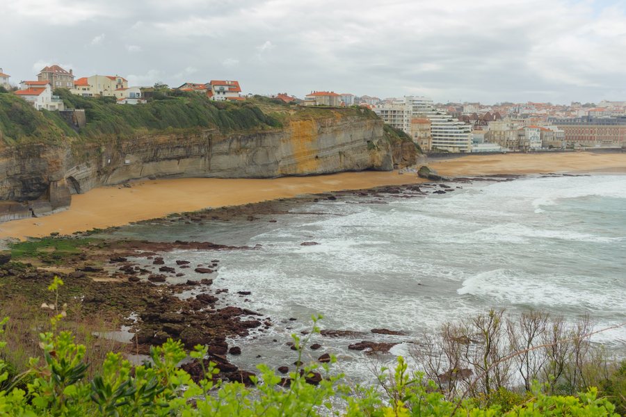 El acantilado de arenisca de la playa Miramar, con las villas de tejado rojo arriba y la ciudad al fondo.